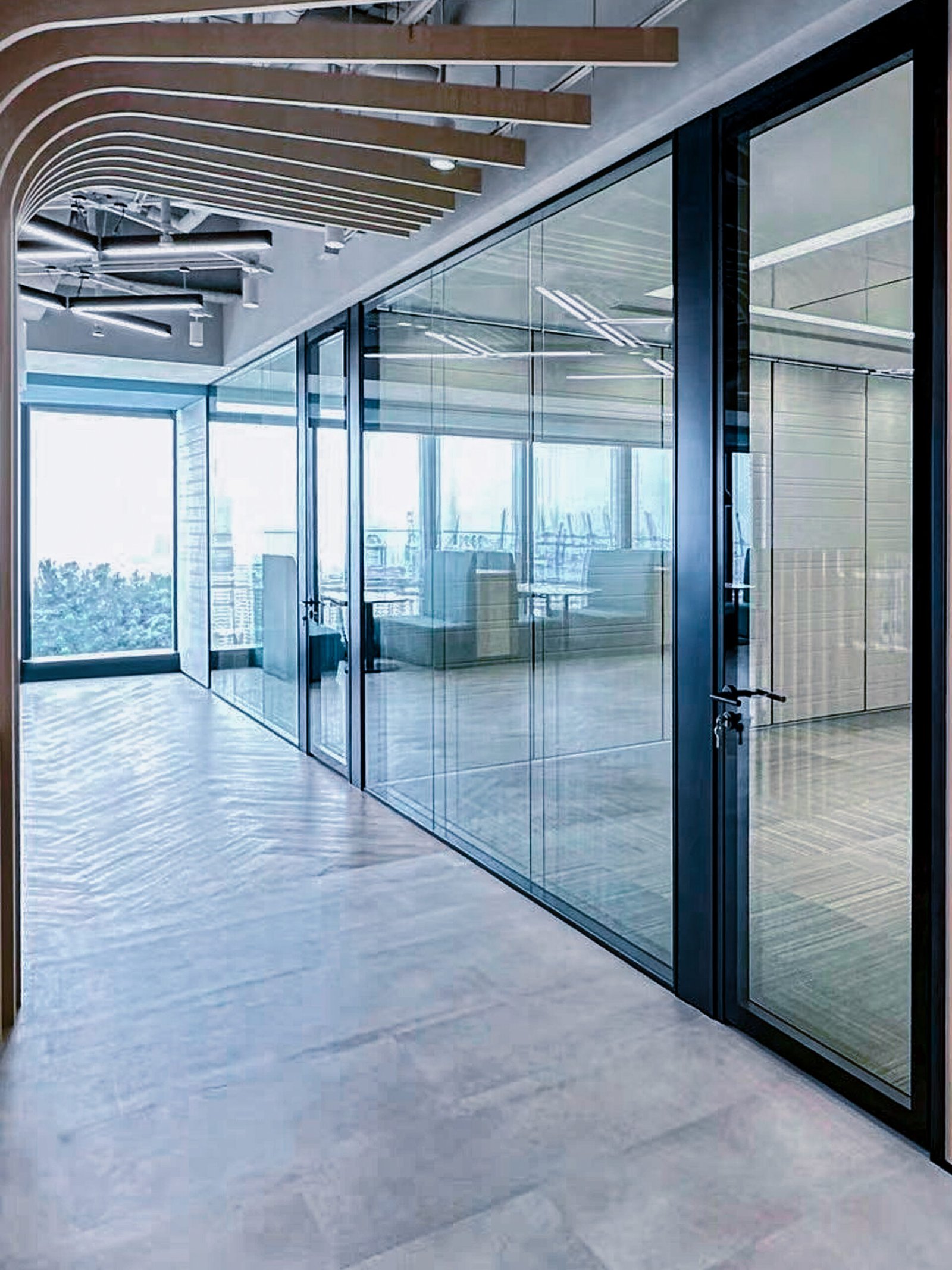 A glass partition system with a matching door creates a sleek and professional office corridor, maximizing light and visibility between the hallway and individual offices.