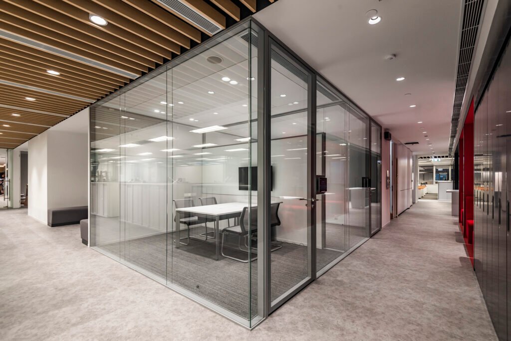 Full-height panoramic double glass partition system creating a transparent private meeting room in an open-plan office.
