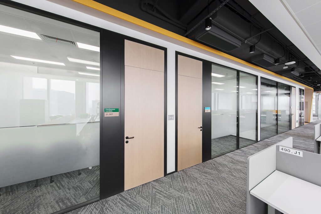 Panoramic glass partition system with light wood door and black aluminum frame for modern office corridors.