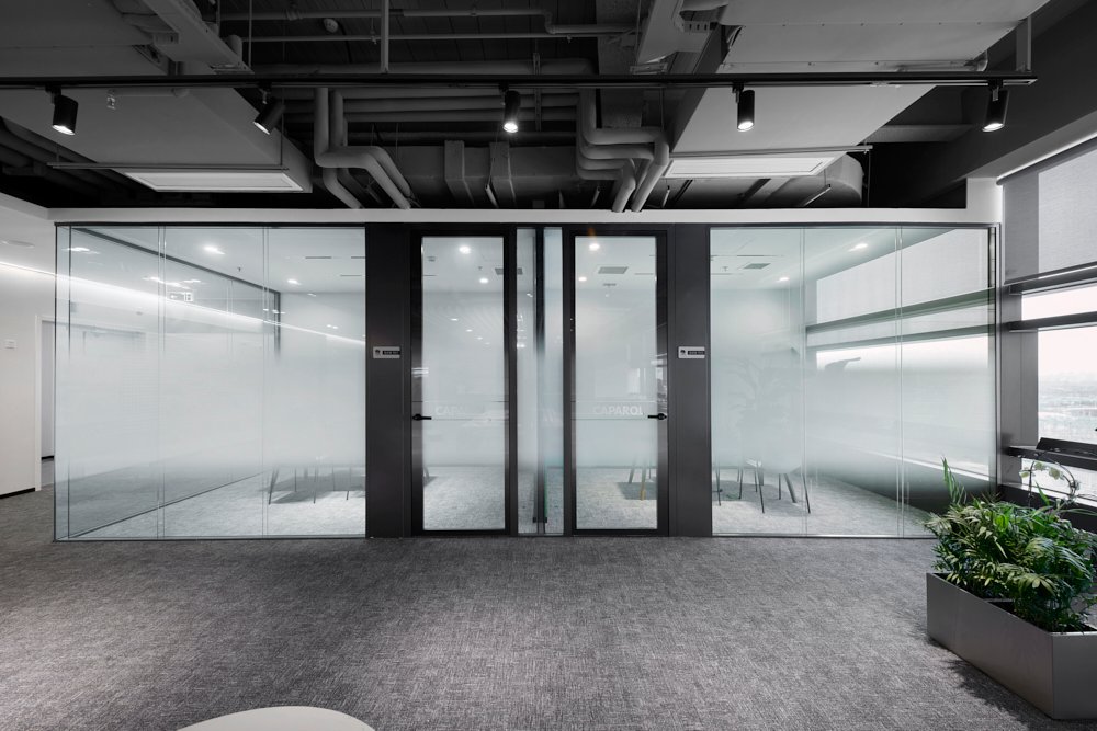 Industrial style office glass partition with frosted privacy film and exposed ceiling design for soundproof workspaces.
